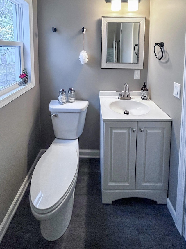 half bath featuring baseboards, vanity, and toilet