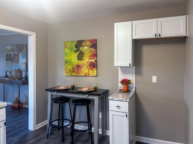 kitchen with dark wood finished floors, tasteful backsplash, white cabinets, light stone countertops, and baseboards