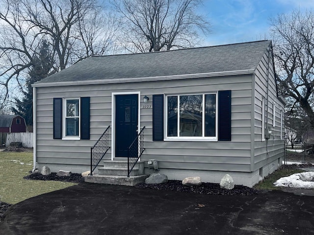 bungalow-style home with entry steps, roof with shingles, and fence