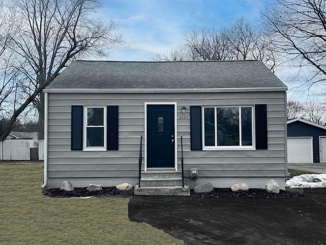 bungalow featuring a shingled roof, entry steps, a garage, an outdoor structure, and a front lawn