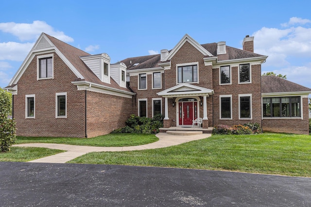 view of front of property with brick siding, a shingled roof, a chimney, and a front yard