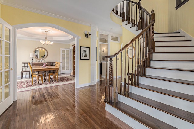 staircase featuring arched walkways, a tray ceiling, ornamental molding, baseboards, and hardwood / wood-style flooring