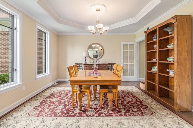 dining space with a tray ceiling, a notable chandelier, ornamental molding, wood finished floors, and baseboards