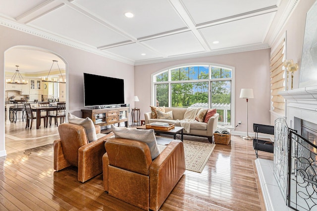 living room featuring arched walkways, coffered ceiling, a fireplace with raised hearth, and light wood-style flooring