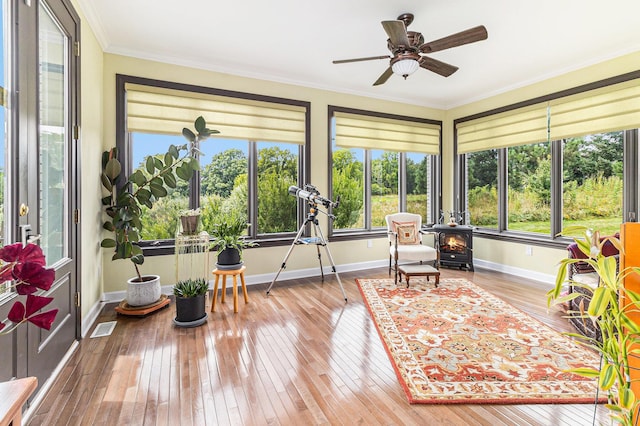 sunroom with a wood stove, visible vents, and a ceiling fan