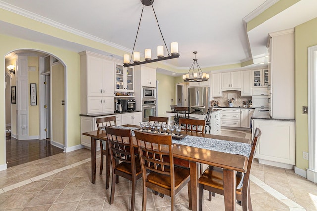 dining space with light tile patterned floors, baseboards, arched walkways, and crown molding