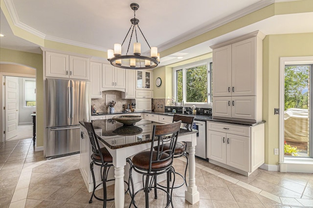 kitchen featuring arched walkways, stainless steel appliances, decorative backsplash, ornamental molding, and a sink