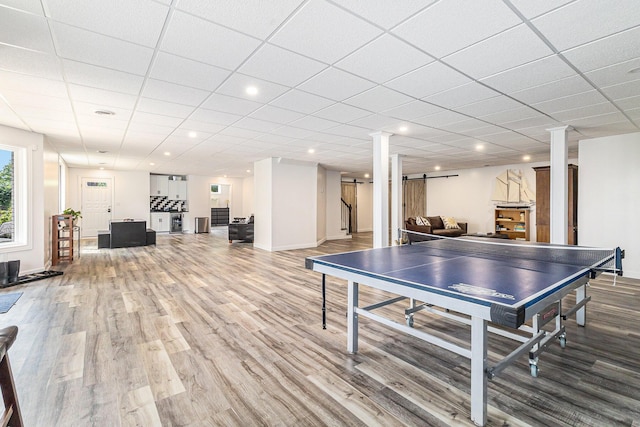 recreation room featuring a barn door, a drop ceiling, recessed lighting, wood finished floors, and baseboards