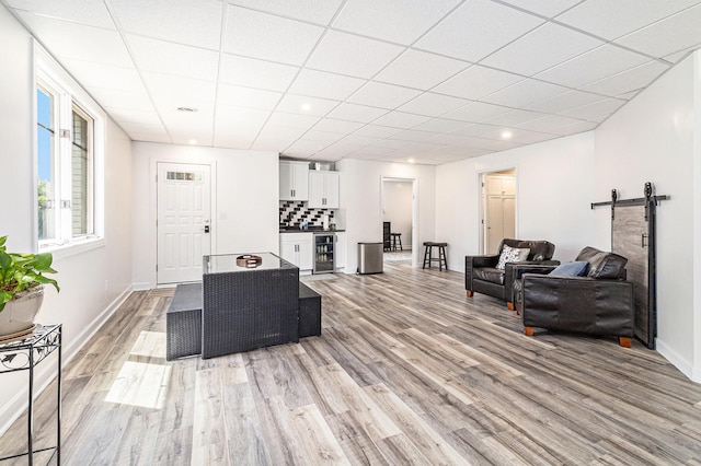 living area featuring beverage cooler, a barn door, light wood finished floors, and a drop ceiling