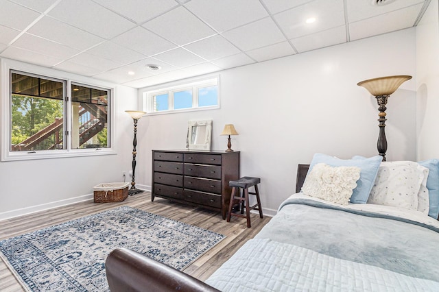 bedroom with a drop ceiling, wood finished floors, and baseboards