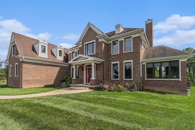 view of front of property featuring a shingled roof, brick siding, a chimney, and a front lawn