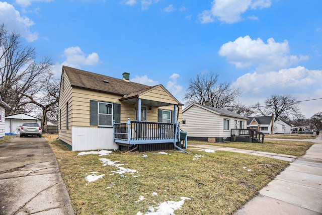 bungalow featuring covered porch, a shingled roof, a front yard, and an outbuilding