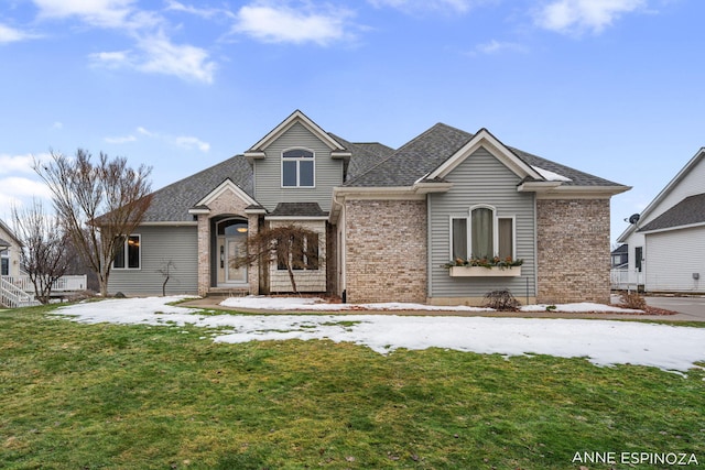 view of front of home featuring a shingled roof, a front lawn, and brick siding