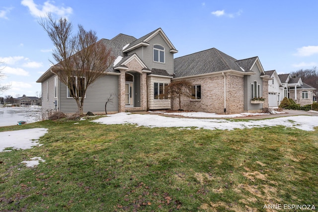 traditional-style house featuring roof with shingles, a front lawn, and brick siding