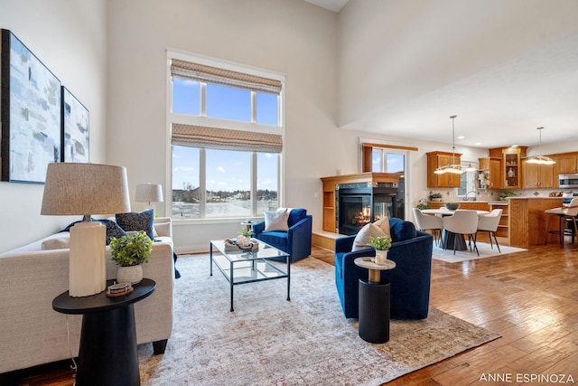 living room featuring a towering ceiling, light wood-style floors, recessed lighting, and a glass covered fireplace