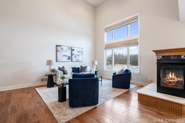 living area featuring a high ceiling, wood-type flooring, a fireplace, and baseboards