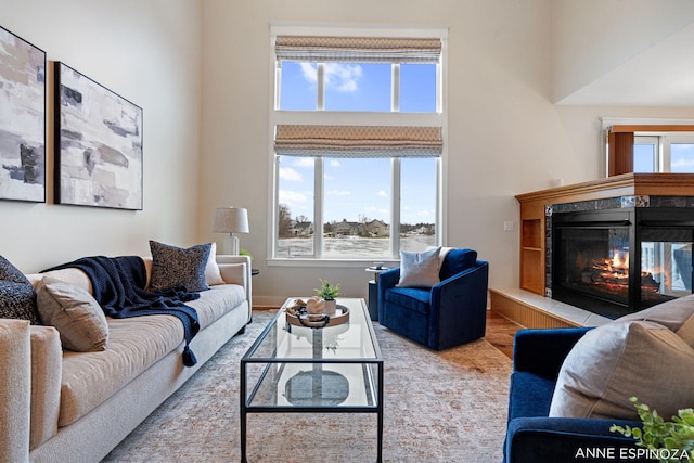 living area with a towering ceiling, a premium fireplace, a wealth of natural light, and wood finished floors