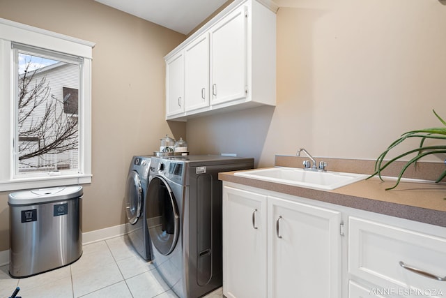 clothes washing area featuring light tile patterned floors, cabinet space, a sink, separate washer and dryer, and baseboards