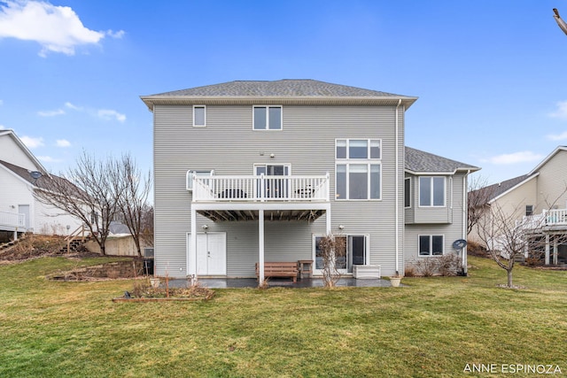 back of property with a wooden deck, a shingled roof, a lawn, and a patio