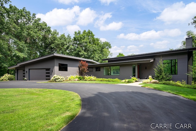 view of front facade featuring a garage, driveway, a chimney, and a front lawn