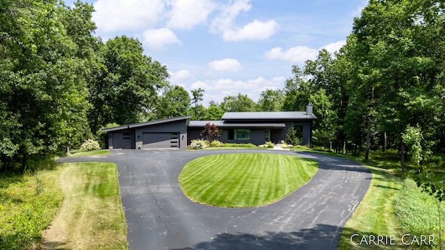 view of front of home with an attached garage, driveway, a chimney, and a front yard