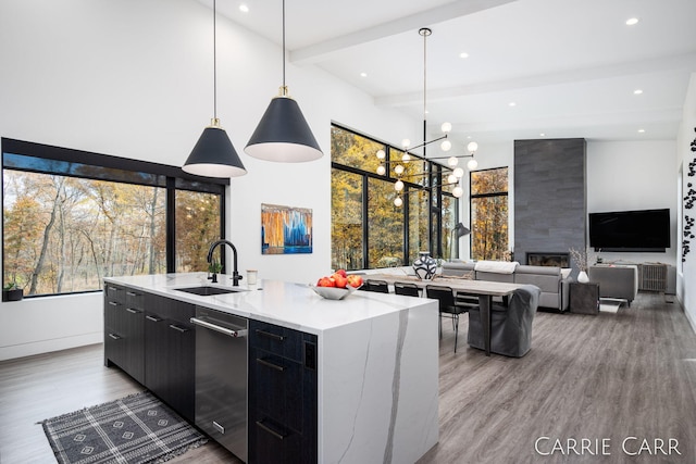 kitchen with modern cabinets, dark cabinets, beamed ceiling, a kitchen island with sink, and a sink