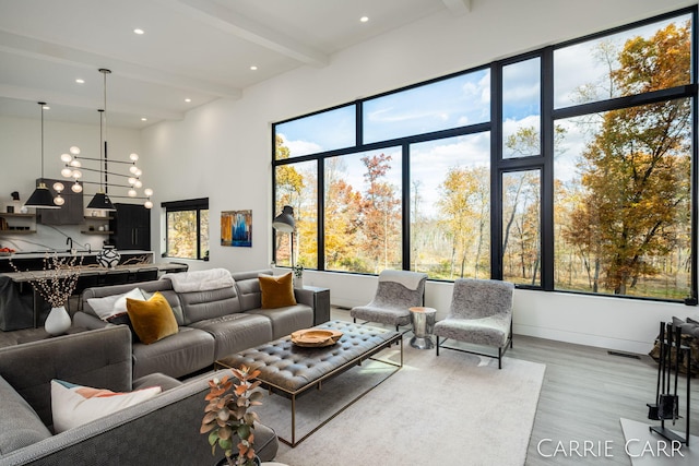 living area with a chandelier, beamed ceiling, a high ceiling, and wood finished floors