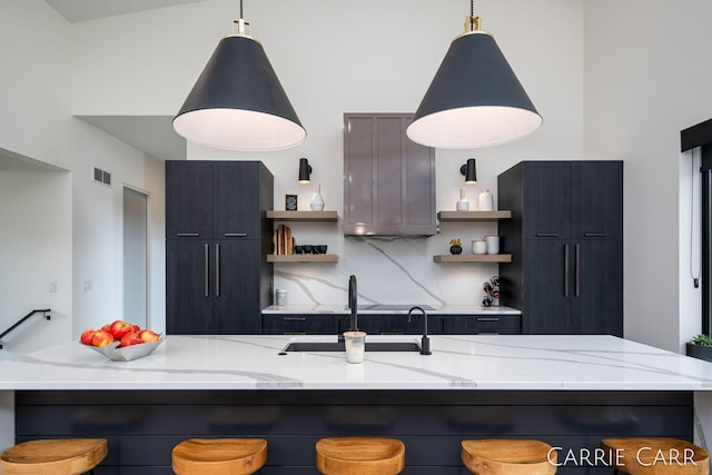 kitchen with light stone countertops, a sink, backsplash, and open shelves