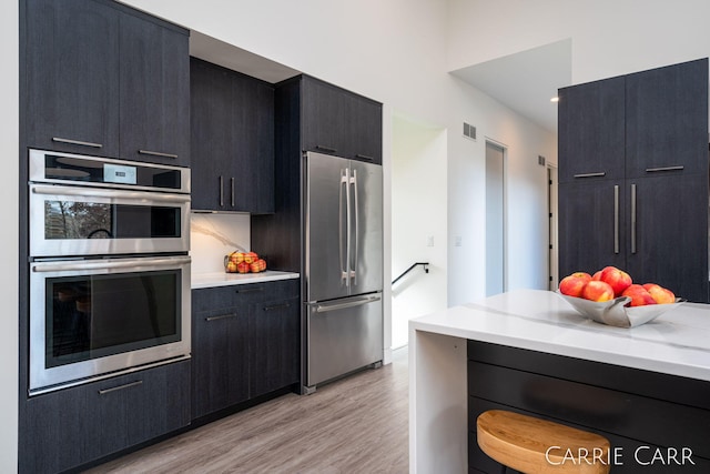 kitchen with light wood finished floors, visible vents, appliances with stainless steel finishes, dark cabinets, and light countertops