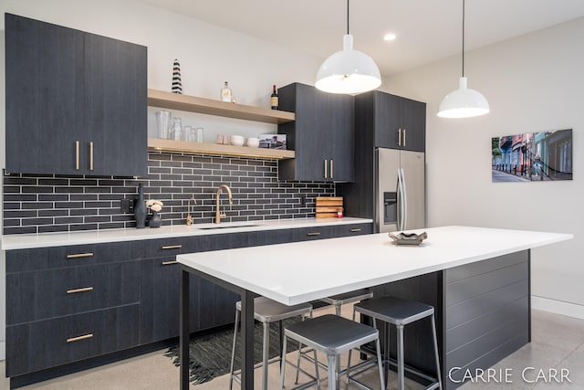 kitchen featuring a breakfast bar area, tasteful backsplash, light countertops, a sink, and stainless steel fridge