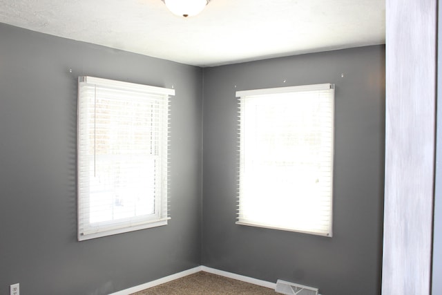 empty room with carpet flooring, visible vents, and baseboards