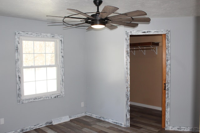 unfurnished bedroom featuring a textured ceiling, dark wood-style flooring, visible vents, baseboards, and a closet