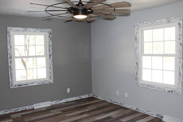 empty room featuring visible vents, dark wood-style flooring, and a wealth of natural light