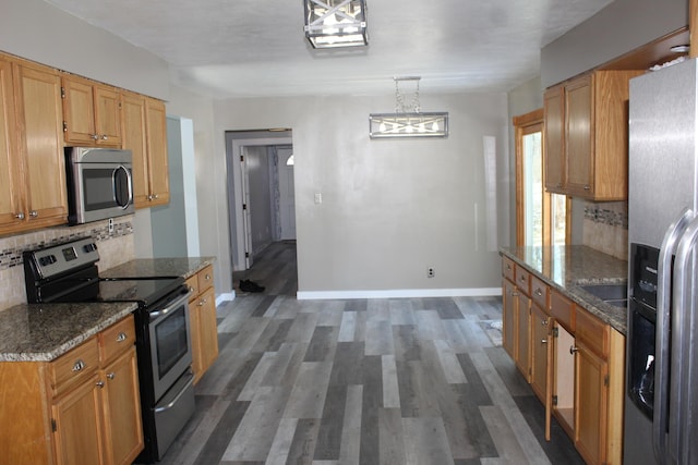 kitchen with baseboards, decorative backsplash, appliances with stainless steel finishes, dark stone countertops, and wood finished floors