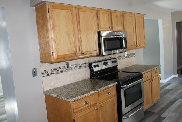 kitchen with appliances with stainless steel finishes, dark stone countertops, dark wood-style floors, and tasteful backsplash