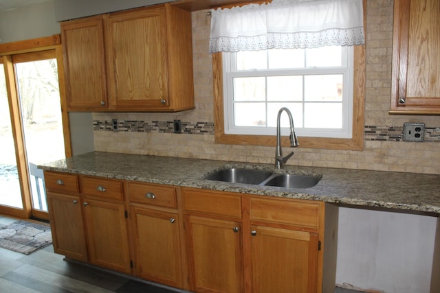 kitchen featuring tasteful backsplash, brown cabinetry, a sink, and light stone countertops