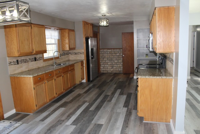 kitchen with appliances with stainless steel finishes, a sink, light stone counters, and wood finished floors