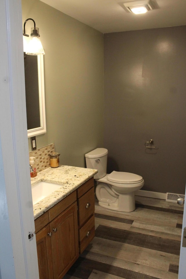 half bathroom with toilet, wood finished floors, visible vents, vanity, and decorative backsplash