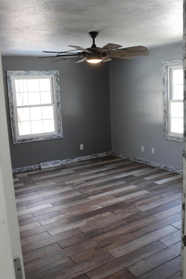 spare room with a textured ceiling, dark wood-style flooring, visible vents, and a ceiling fan