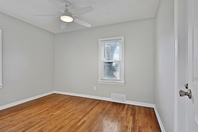 empty room featuring a textured ceiling, hardwood / wood-style flooring, a ceiling fan, visible vents, and baseboards