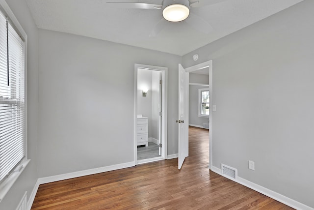 unfurnished bedroom with visible vents, ceiling fan, connected bathroom, wood finished floors, and baseboards