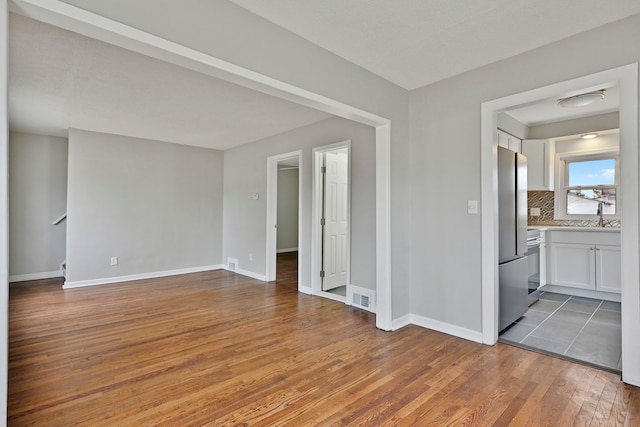 unfurnished room with visible vents, baseboards, wood-type flooring, stairway, and a sink