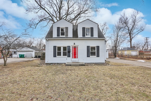 dutch colonial featuring roof with shingles, a front yard, fence, and an outbuilding