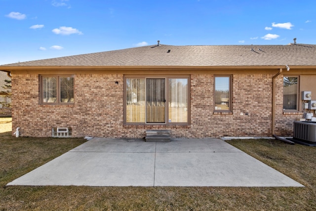 back of property with brick siding, central air condition unit, roof with shingles, a lawn, and a patio area