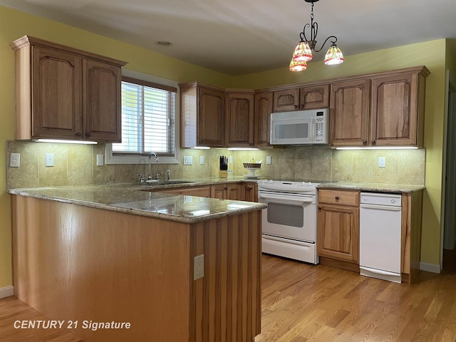 kitchen with a peninsula, white appliances, a sink, hanging light fixtures, and light wood finished floors