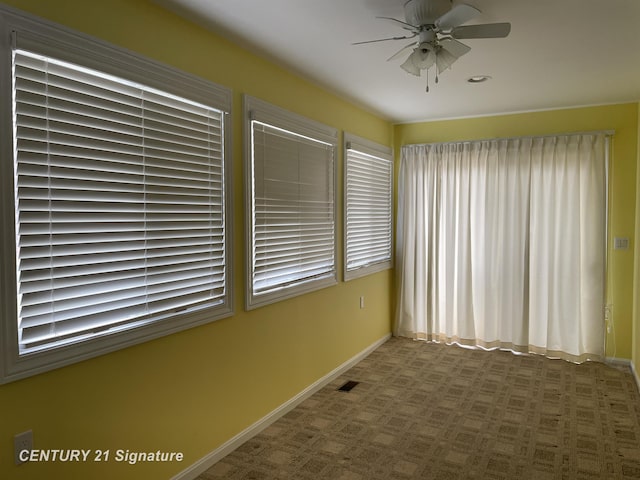 unfurnished room with baseboards, a ceiling fan, visible vents, and a wealth of natural light