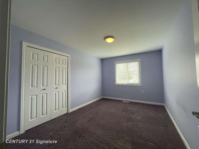 unfurnished bedroom featuring baseboards, dark carpet, and a closet