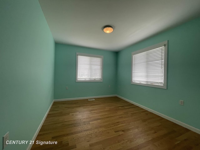 spare room featuring a wealth of natural light, wood finished floors, and baseboards