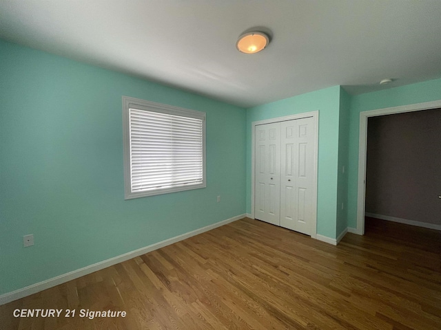 unfurnished bedroom featuring baseboards, wood finished floors, and a closet
