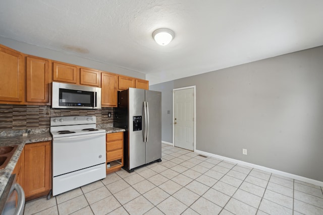 kitchen with appliances with stainless steel finishes, light tile patterned flooring, backsplash, and baseboards